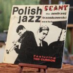 Płyta winylowa w papierowej okładce. Seant – Polish Jazz Vol. 11. [Sient – Polisz Dżez] Andrzej Trzaskowski Sextet. Wytwórca: Muza Polskie Nagrania. Polska – tysiąc dziewięćset sześćdziesiąt dwa. Wymiary: płyta o średnicy trzydziestu centymetrów, koperta kwadratowa o boku trzydzieści na trzydzieści centymetrów. Płyta w kopercie ustawiona na drewnianym stojaku. Na białym tle czarno-białe szkice sylwetek: po prawej stronie mężczyzny grającego na trąbce, po lewej, plecami do trębacza sylwetka mężczyzny przy fortepianie. Od góry napisy z tytułem płyty, w narożniku płyty znajdującym się z prawej strony fotografii logo wytwórni i numer katalogowy: XL zero-trzy -siedem-osiem. W pobliży narożnika płyty znajdującego się po lewej stronie fotografii czerwony napis: featuring Ted Curson [Ficzering Ted Karson].