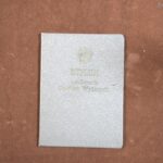 Okładka, białoczarne marmurkowanie, od góry, wyśrodkowane, w kolorze złotym, odcisk godła Polski z okresu peerelu, orzeł bez korony, pod spodem odciśnięty i w złotym kolorze napis dyplom ukończenia studiów wyższych, z nałożonym od lewej strony odciskiem pieczęci okrągłej z orłem w centralnym położeniu.