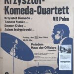 Plakat koncertowy. Druk na papierze. Poczdam – Niemcy, rok tysiąc dziewięćset sześćdziesiąty szósty. Wymiary sześćdziesiąt jeden na osiemdziesiąt sześć centymetrów. Od góry plakatu napisy: Jazzkonzert [Dżezkoncert ] des Monats. Pod spodem Krzysztof Komeda Quartett. Krzysztof Komeda, Tomasz Stańko, Roman Dyląg, Adam Jędrzejowski. Pod naposami monochromatyczny niebieskawy nadruk sylwetki mężczyzny siedzącego przy zestawie perkusyjnym. Z prawej strony plakatu wycięty fragment artykułu prasowego ze zdjęciem Adama Jarzębowskiego.