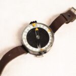 Busola wyprodukowana w Związku Socjalistycznych Republik Sowieckich w latach trzydziestych dwudziestego wieku. Okrągła busola ze szklanym wieczkiem na skórzanym pasku umożliwiającym zapięcie jej na nadgarstku. Na przezroczystym wieczku żółte trójkąty umieszczone naprzeciwko siebie, przy jednym muszka, przy drugim szczerbinka. Pod przezroczystym, szklanym wieczkiem wskazówka i limbus (pierścień z podziałką) z podwójnym skalowaniem i żółtym trójkątem umieszczonym na pozycji trzystu sześćdziesięciu stopni.