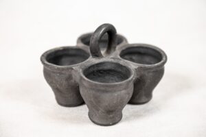 Czworak. Twórca: Stanisław Stępowski. Materiał: glina wypalana. Poczwórne, gliniane naczynie. Cztery zwężające się do dołu czarki połączone ze sobą. W miejscu łączenia gliniany pałąk.