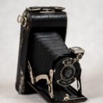 Aparat fotograficzny Kodak Vollenda sześćset dwadzieścia. Produkcja: Stany Zjednoczone, lata trzydzieste dwudziestego wieku. To aparat mieszkowy. Obiektyw wysuwany na harmonijkowym mieszku łączącym obiektyw z korpusem aparatu. Korpus metalowy pokryty czarna skórą z chromowanymi sprzączkami. Na pierścieniu obiektywu napisy: KODO, EKC 620, MADE IN USA [Mejd in Ju eS eJ] EASTMAN KODAK CO. [Istman Kodak Kompany] . Z prawej strony aparatu - mechanizm chowania i wysuwania mieszka metalowy, chromowany. U dołu pokrywa, która po schowaniu mieszka zamykała całość i chroniła obiektyw.