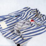 Pasiak z obozu koncentrasyjnego Gross Rosen [ Gros Rozen] z lat czterdziestych dwudziestego wieku. Bluza i czapka z pasiaka z obozu koncentracyjnego. Bluza ma pionowe, niebieskie paski, czapka również, ale nieco bardziej spłowiałe. Bluza z długimi rękami i miękkim kołnierzykiem, zapinana na guziki. Na wysokości serca po lewej stronie bluzy naszyta prostokątna łata z literą P na czerwonym, trójkątnym tle i numerem: siedemdziesiąt tysięcy sześćdziesiąt. W dolnej części bluzy z prawej strony – biała, prostokątna łata.