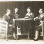 Siostry Madzińskie: Ania, Wiktoria, Cecylia, Monika. Fotografia – sepia. Autor nieznany, wymiary: trzynaście i osiem dziesiątych na osiem i siedem dziesiątych centymetra, czas powstania – lata dwudzieste dwudziestego wieku. Wnętrze pomieszczenia, cztery kobiety siedzą w wiklinowych fotelach przy wiklinowym stole na tle ciemnej kotary. Dwie lekko z przodu, dwie lekko z tyłu, część ich sylwetek ukryta za stołem. Te z przodu mają na sobie plisowane spódnice do połowy łydki i ciemne buty z paskiem przez górną część stopy. Wszystkie mają na sobie żakiety z wykładanymi kołnierzykami.