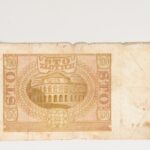 Rewers: Zadrukowane dwie trzecie powierzchni banknotu. Po lewej i prawej stronie nominały: liczbowo i słownie, w centralnej części w rozecie giloszowej budynek z kolumnadą i kopułą: budynek Banku Polskiego w Warszawie z tysiąc osiemset dwudziestego ósmego roku. Na niezadrukowanej części zagniecenia i lekkie przybrudzenia.